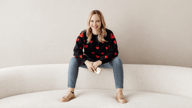 Woman with long blonde hair in a heart-patterned sweater sitting on a couch
